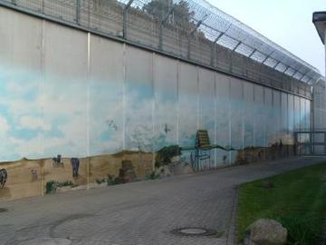 Foto, dass einen Blick auf die von Gefangenen bemalte Außenmauer zur Bahnseite zeigt (Zum Artikel über die Hauptanstalt). Suchsymbol Lupe
