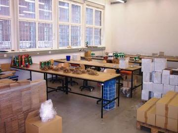 Foto eines Werkbereiches, dass mehrere Arbeitsplätze zeigt, an denen für Unternehmen Sortier- und Verpackungsarbeiten durchgeführt werden (Zum Artikel über die Hauptanstalt). Suchsymbol Lupe