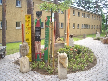 Foto des Weges zum Kunstbereich, verziert mit bearbeiteten Sandsteinen und auf Holzbrettern geschriebenen Lebensweisheiten (Zum Artikel über die Abteilung Lingen-Damaschke). Suchsymbol Lupe