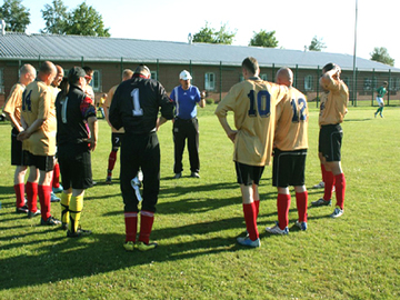 Das Foto zeigt Gefangene mit ihrem Trainer bei der Teambesprechung kurz vor Anstoß eines Punktspieles (Zum Artikel Sport- und Freizeitangebote)