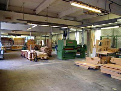 Foto des Innenbereiches der Tischlerei, dass eine CNC-Maschine und diverse andere Maschinen nebst Material zeigt (Zum Artikel Tischlerei)